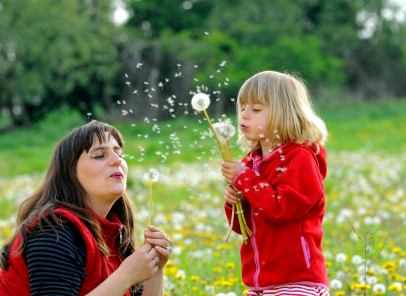 little girl blowing dandelion with mom in park